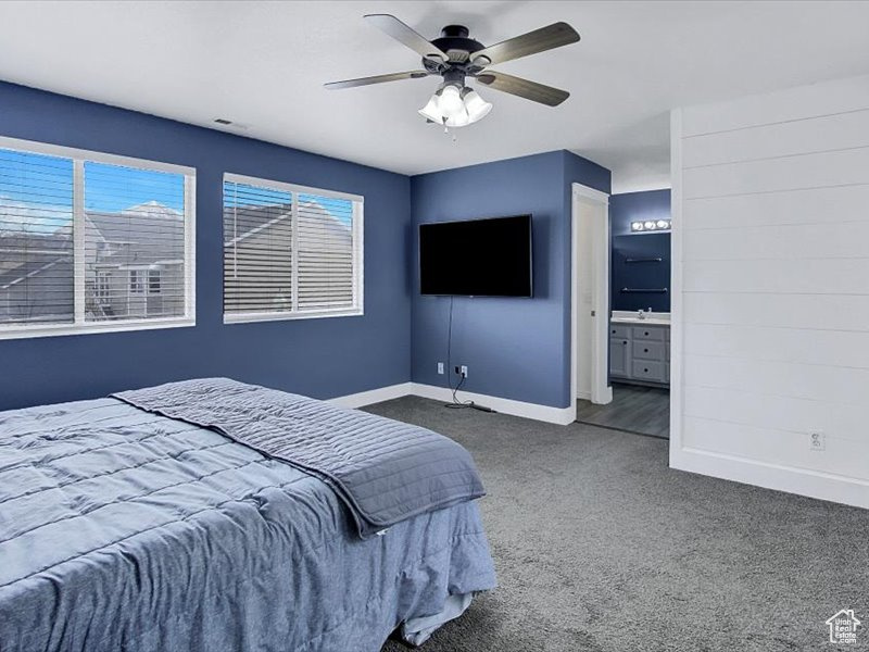 Bedroom featuring ensuite bathroom, ceiling fan, dark colored carpet, and multiple windows