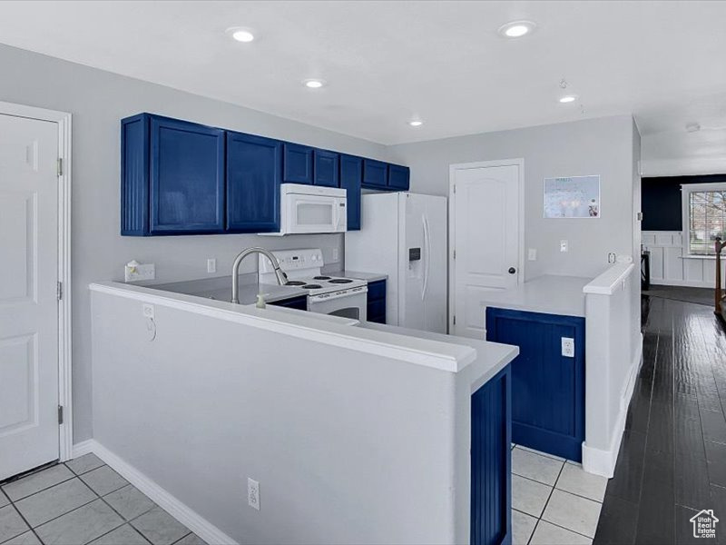 Kitchen with kitchen peninsula, sink, blue cabinetry, white appliances, and light wood-type flooring