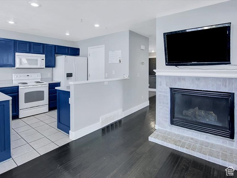 Kitchen featuring white appliances, blue cabinetry, a tiled fireplace, and light hardwood / wood-style floors