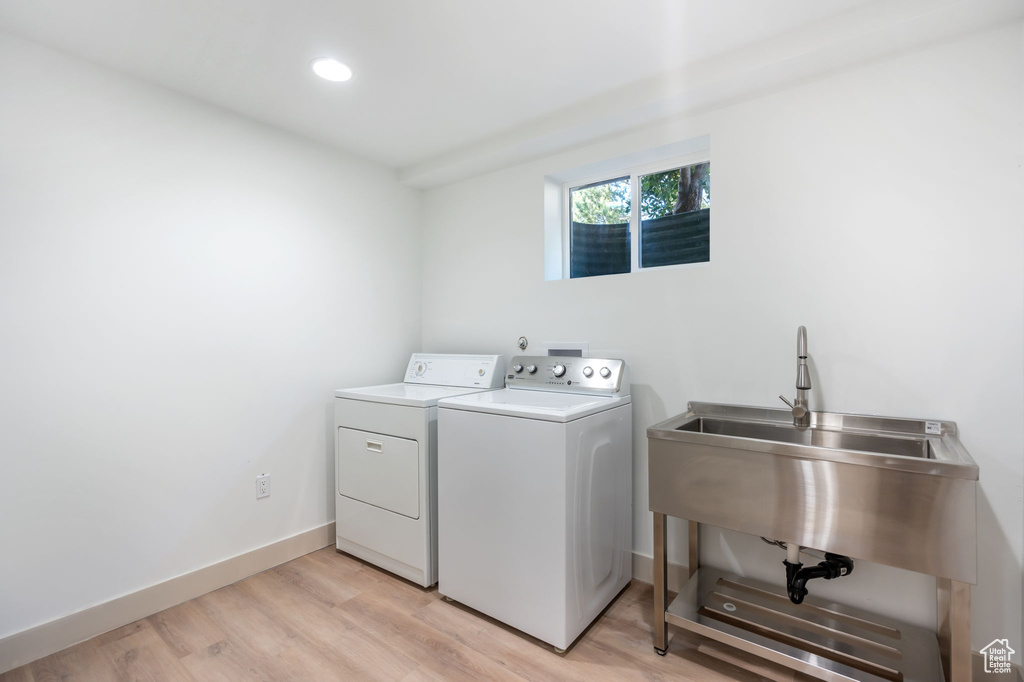 Clothes washing area with washing machine and clothes dryer and light hardwood / wood-style flooring