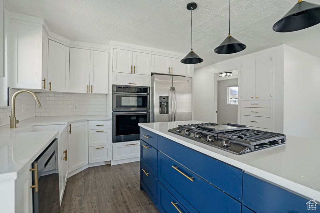 Kitchen with dark hardwood / wood-style flooring, appliances with stainless steel finishes, blue cabinets, backsplash, and hanging light fixtures