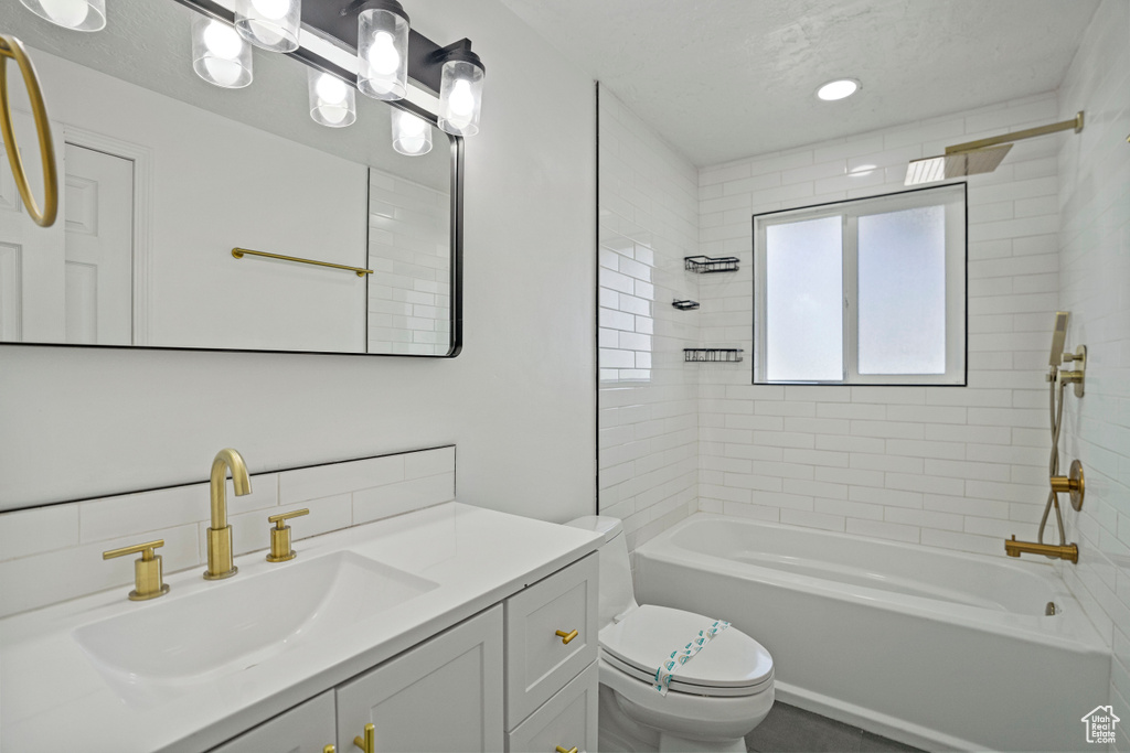 Full bathroom featuring toilet, tiled shower / bath combo, vanity, and a textured ceiling