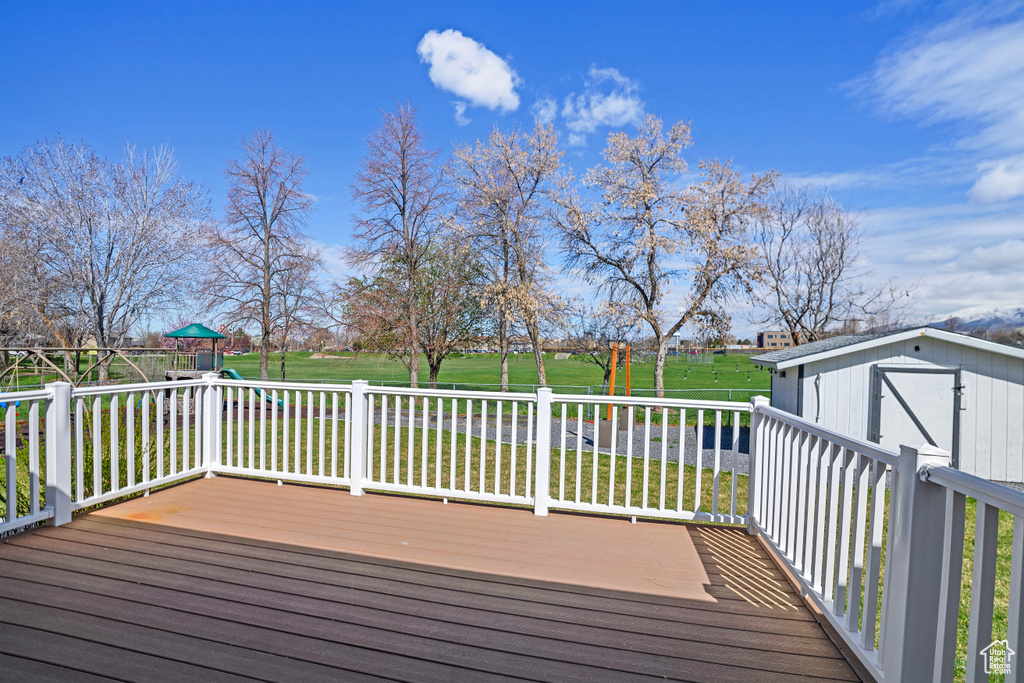 Wooden deck featuring a lawn, a storage unit, and a playground