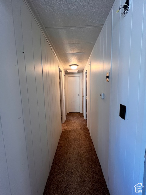 Hallway with a textured ceiling and dark colored carpet