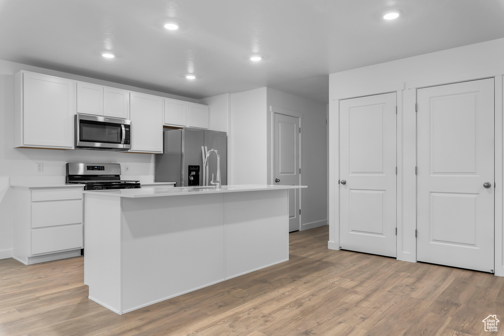 Kitchen featuring white cabinets, appliances with stainless steel finishes, light hardwood / wood-style floors, and a kitchen island with sink