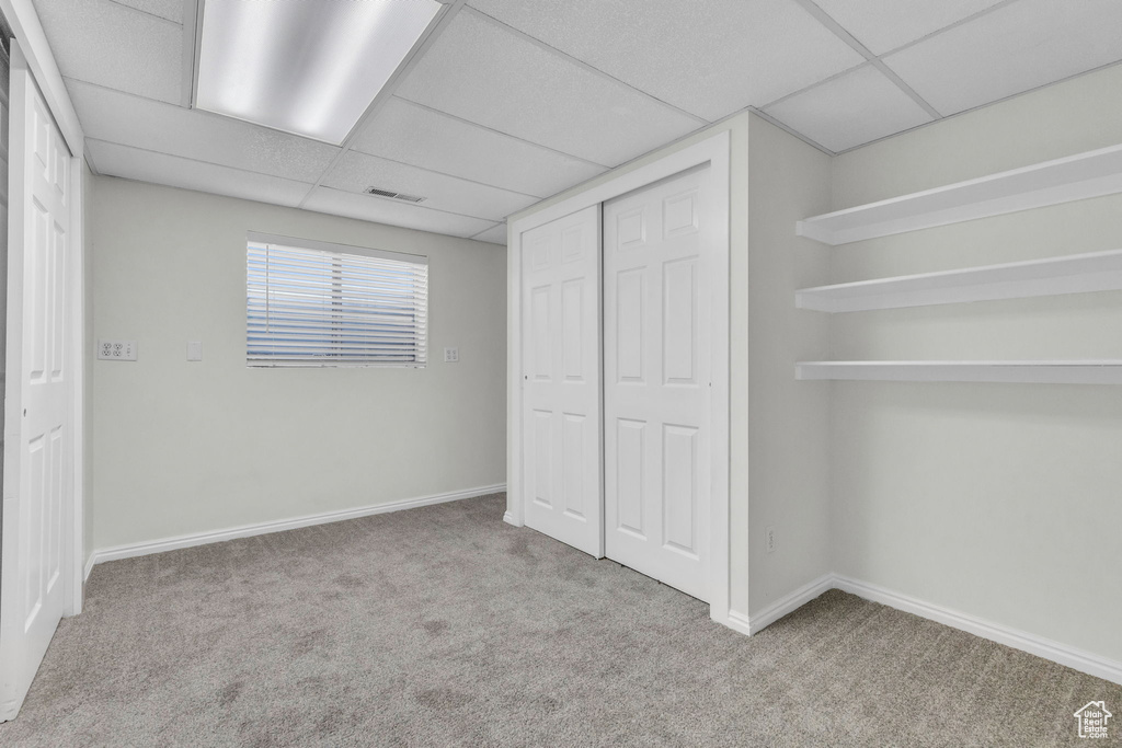 Unfurnished bedroom with a drop ceiling, light carpet, and a closet