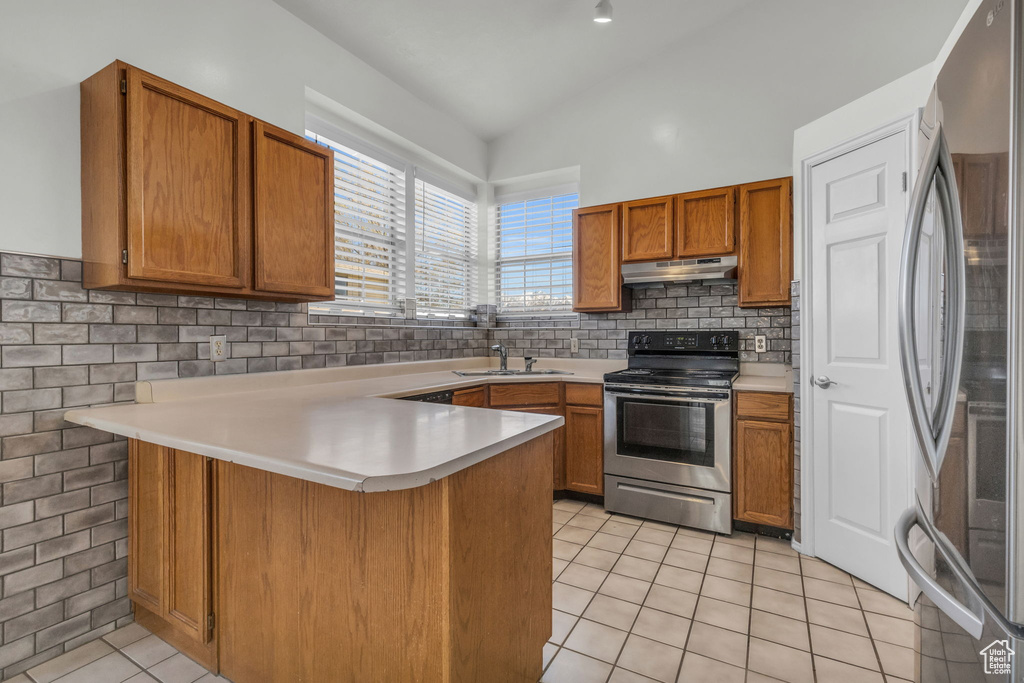 Kitchen with kitchen peninsula, stainless steel appliances, vaulted ceiling, light tile floors, and tasteful backsplash