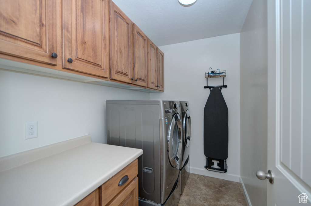 Clothes washing area featuring separate washer and dryer, cabinets, and light tile floors