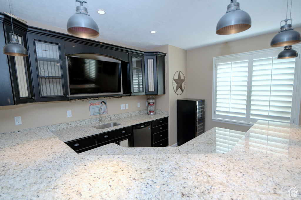 Kitchen featuring decorative light fixtures, stainless steel dishwasher, sink, and light stone counters