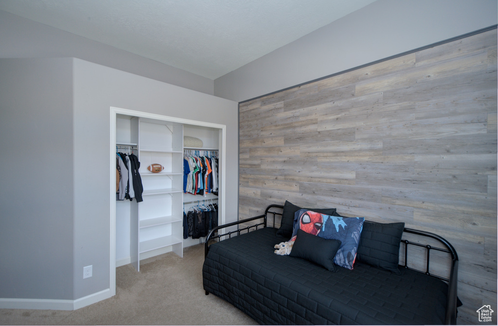 Bedroom featuring a closet, light carpet, and wood walls