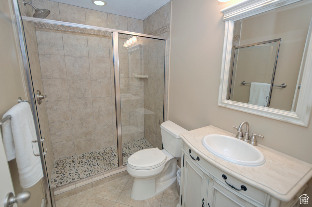 Bathroom featuring a shower with door, toilet, tile flooring, and vanity