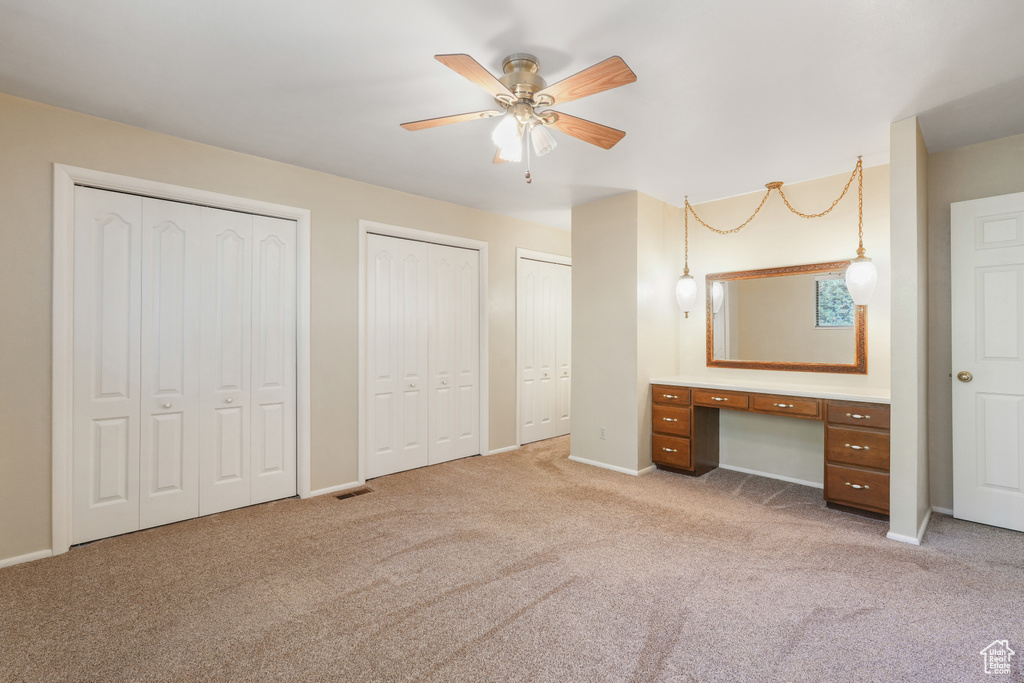Unfurnished bedroom featuring ceiling fan, two closets, carpet, and built in desk