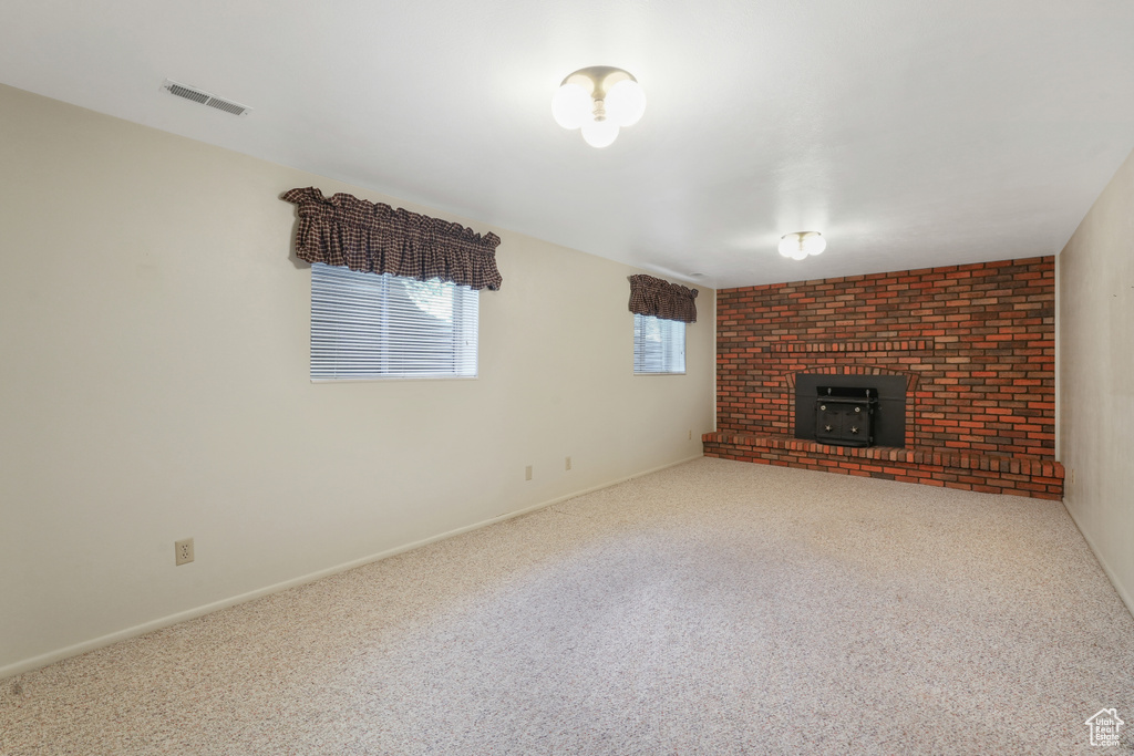 Unfurnished living room featuring light colored carpet, brick wall, and a brick fireplace