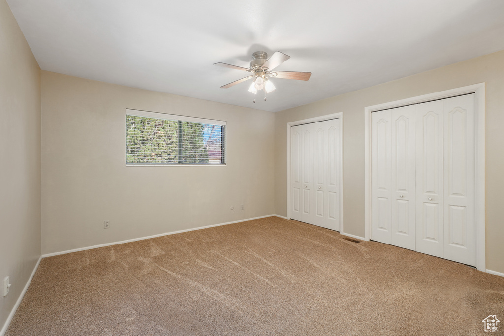 Unfurnished bedroom with ceiling fan, two closets, and light carpet