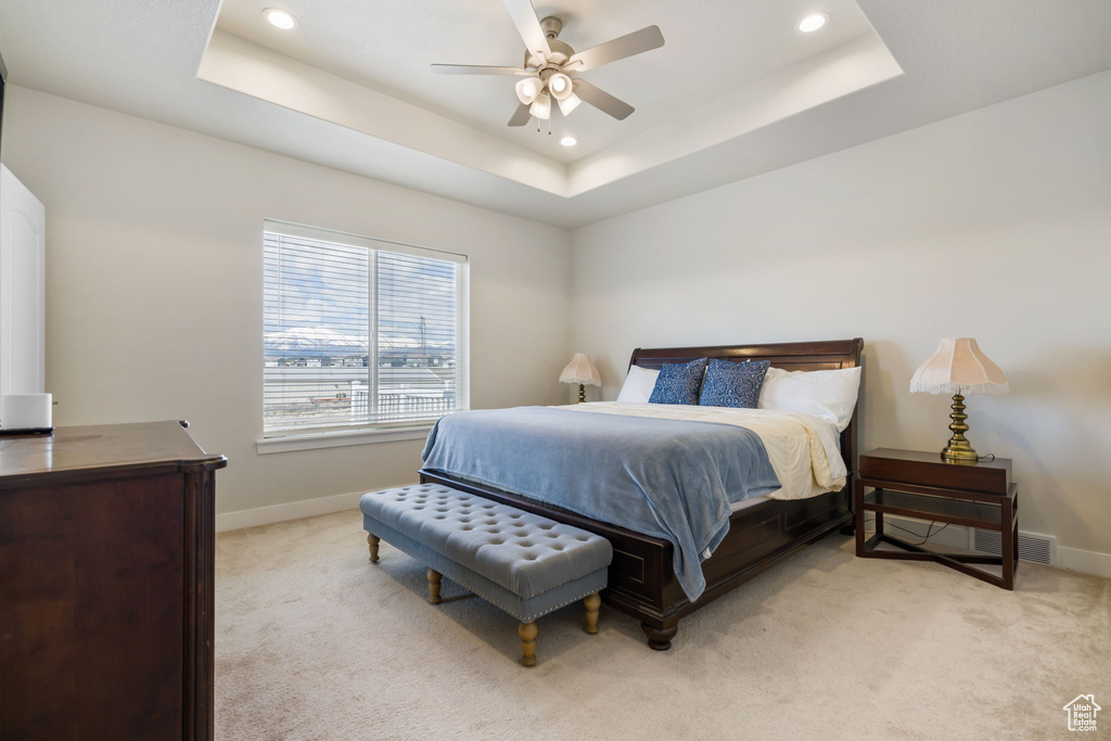 Bedroom featuring ceiling fan, light colored carpet, and a tray ceiling