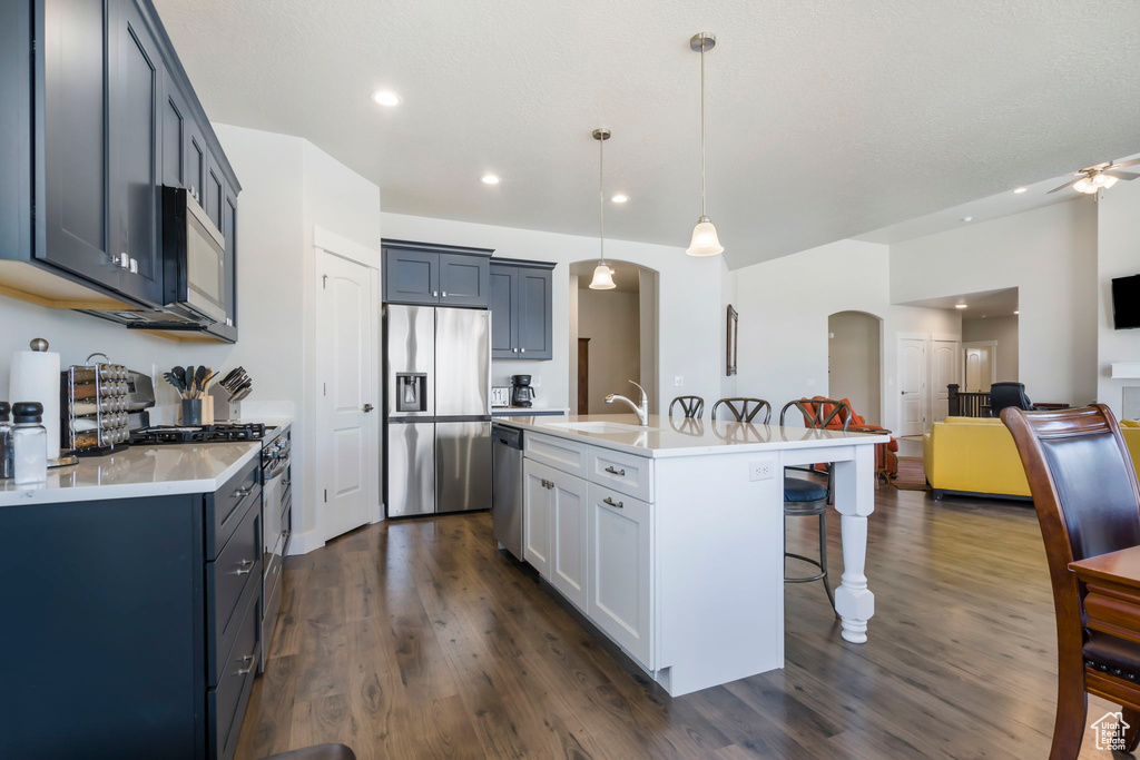 Kitchen featuring decorative light fixtures, dark hardwood / wood-style flooring, stainless steel appliances, a kitchen island with sink, and ceiling fan