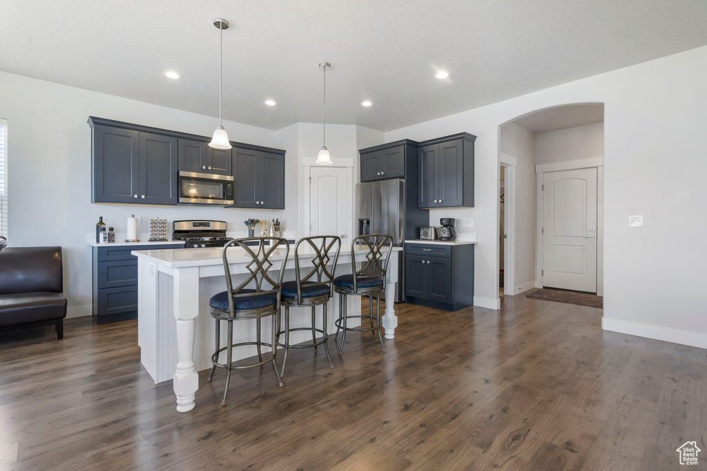 Kitchen featuring stainless steel appliances, dark hardwood / wood-style flooring, an island with sink, a breakfast bar area, and hanging light fixtures