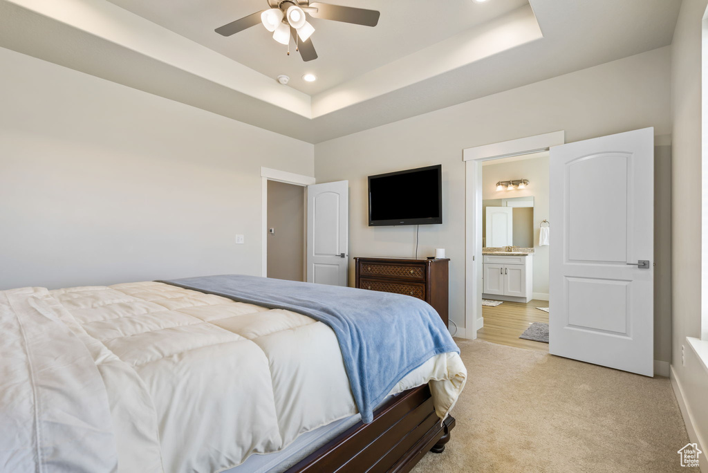 Bedroom with ceiling fan, a tray ceiling, light carpet, and ensuite bathroom