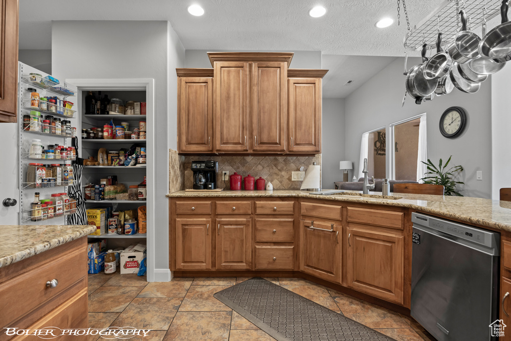 Kitchen with light stone countertops, dishwasher, light tile floors, and tasteful backsplash