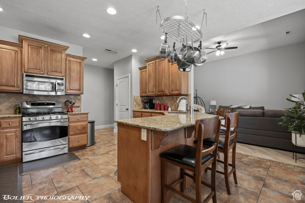 Kitchen featuring ceiling fan with notable chandelier, appliances with stainless steel finishes, light tile flooring, and tasteful backsplash