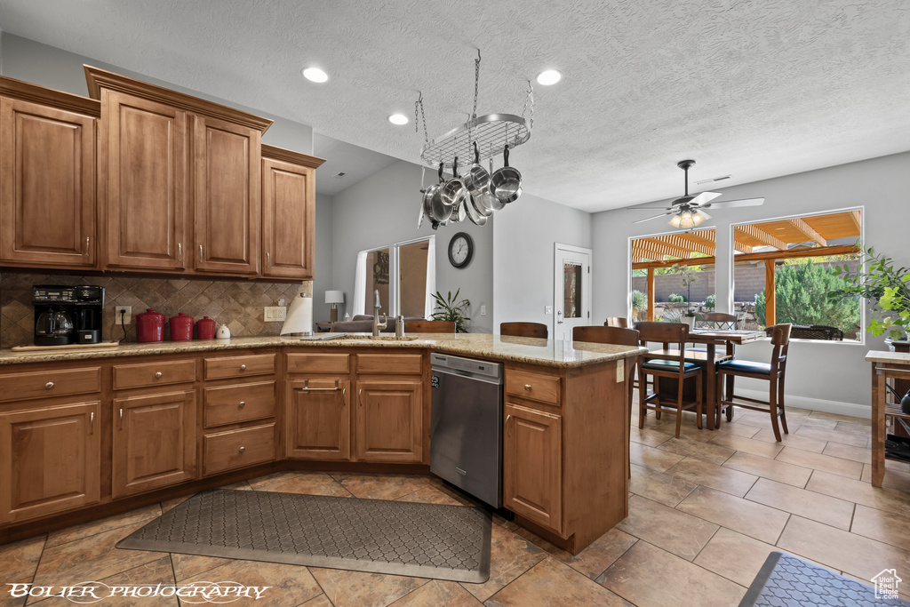 Kitchen featuring dishwasher, kitchen peninsula, light stone counters, tasteful backsplash, and ceiling fan with notable chandelier