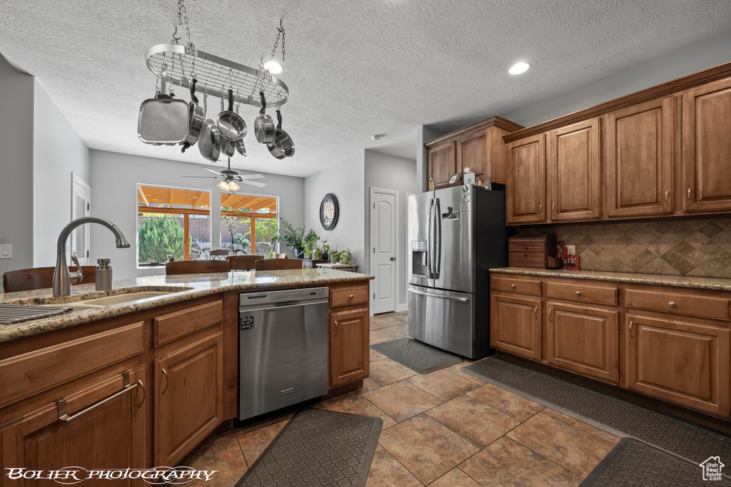 Kitchen featuring backsplash, appliances with stainless steel finishes, sink, tile floors, and ceiling fan with notable chandelier