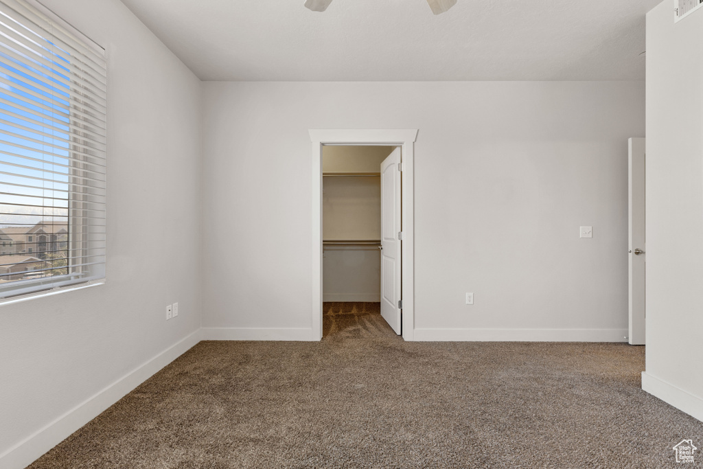 Unfurnished bedroom featuring ceiling fan, a spacious closet, dark carpet, and a closet