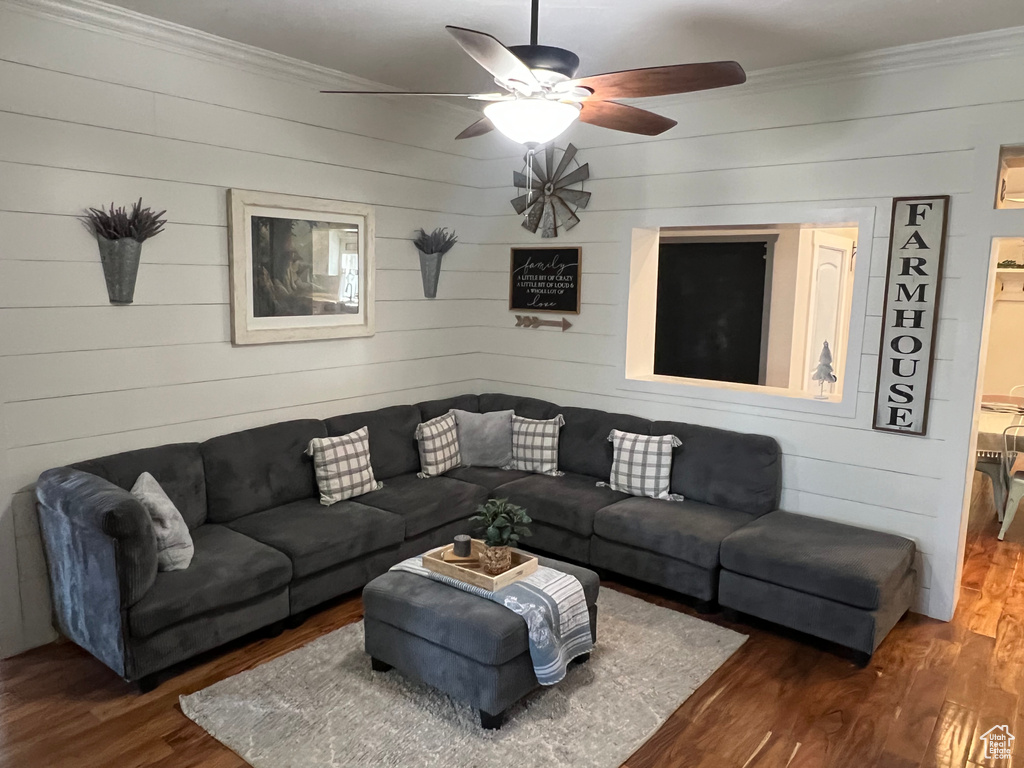Living room featuring ceiling fan, ornamental molding, dark hardwood / wood-style floors, and wooden walls