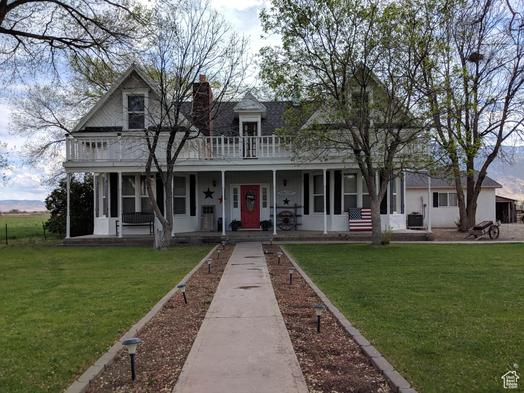View of front of house featuring a front lawn, a balcony, and a porch