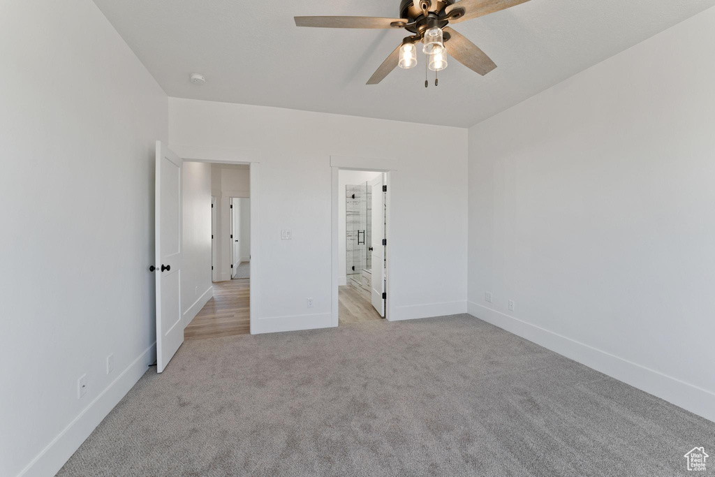 Unfurnished bedroom with ceiling fan, light colored carpet, and ensuite bath