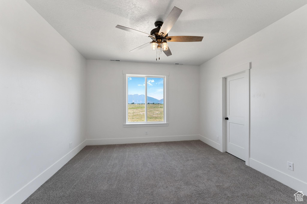 Empty room featuring ceiling fan and dark colored carpet