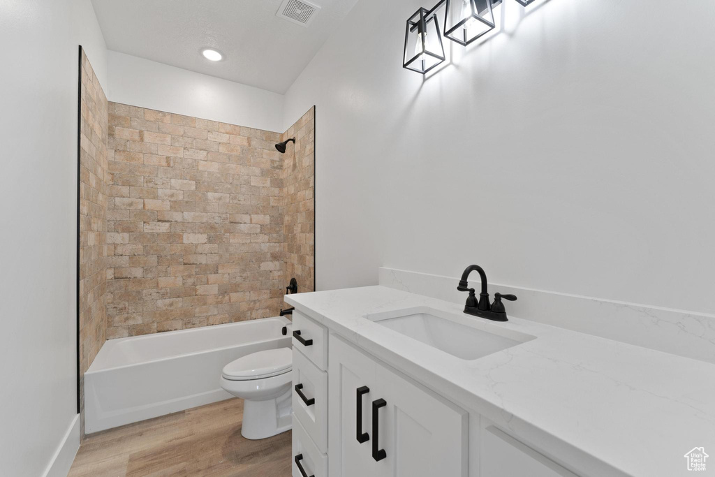 Full bathroom featuring tiled shower / bath combo, toilet, hardwood / wood-style floors, and vanity