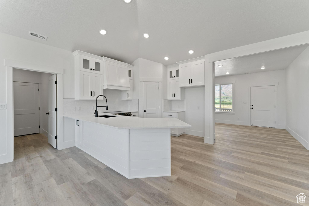 Kitchen with light hardwood / wood-style floors, white cabinets, kitchen peninsula, backsplash, and sink