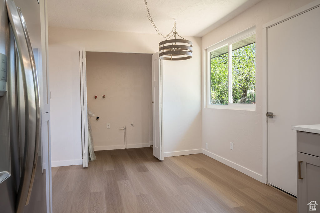 Unfurnished bedroom featuring light hardwood / wood-style flooring, an inviting chandelier, and stainless steel fridge with ice dispenser