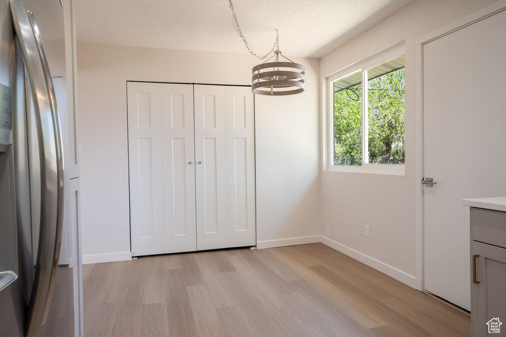 Unfurnished bedroom with an inviting chandelier, a closet, light wood-type flooring, and stainless steel fridge
