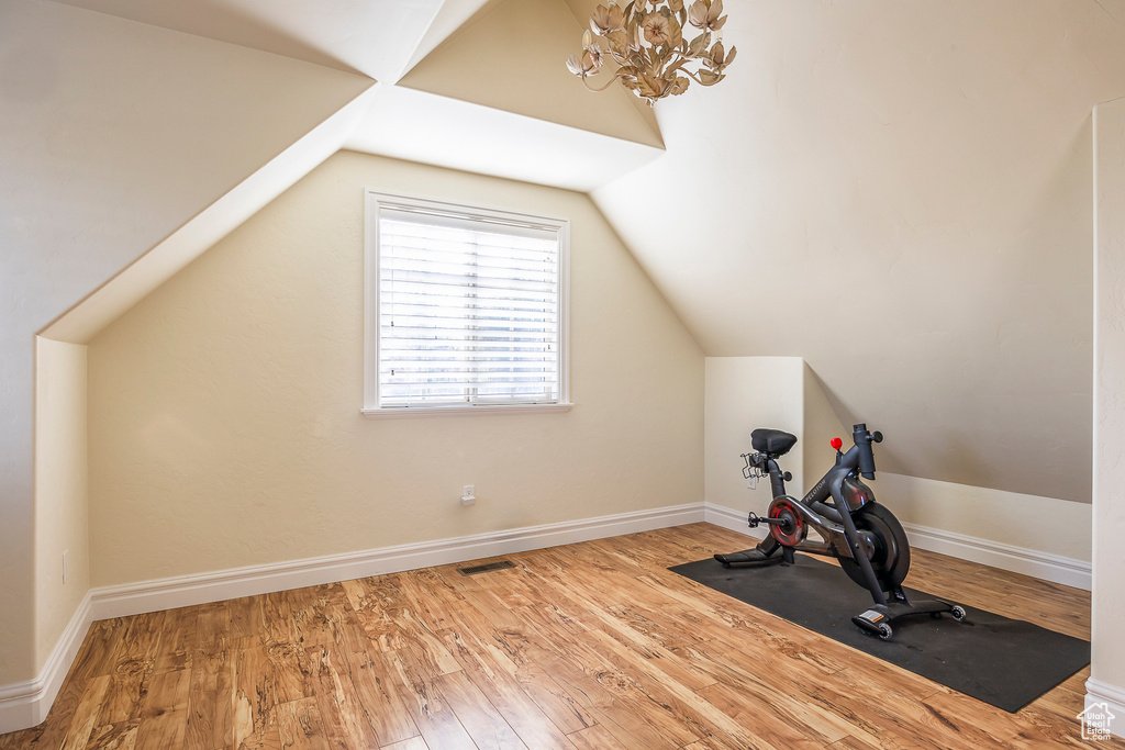 Exercise area featuring an inviting chandelier, light hardwood / wood-style floors, and vaulted ceiling