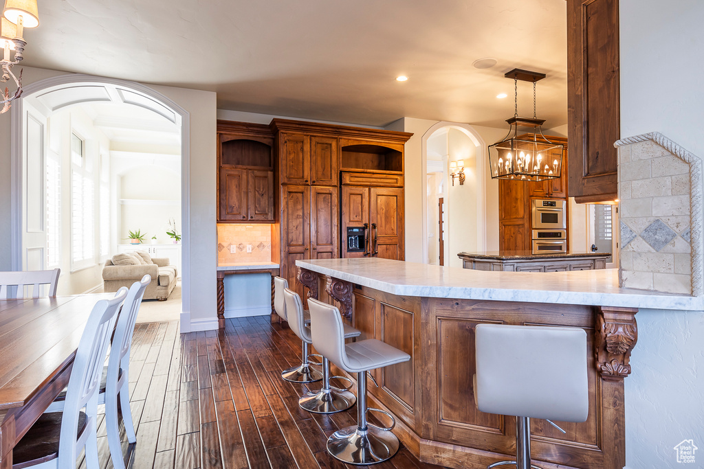 Kitchen featuring a notable chandelier, dark hardwood / wood-style floors, tasteful backsplash, and a kitchen breakfast bar