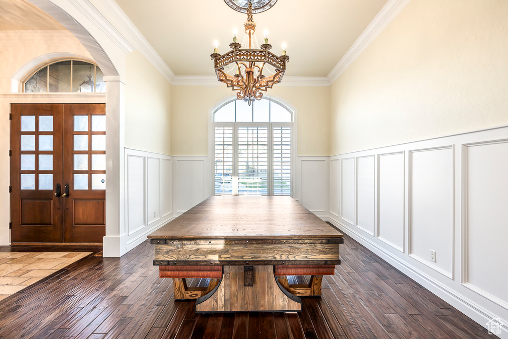 Unfurnished dining area featuring a notable chandelier, ornamental molding, dark wood-type flooring, and french doors