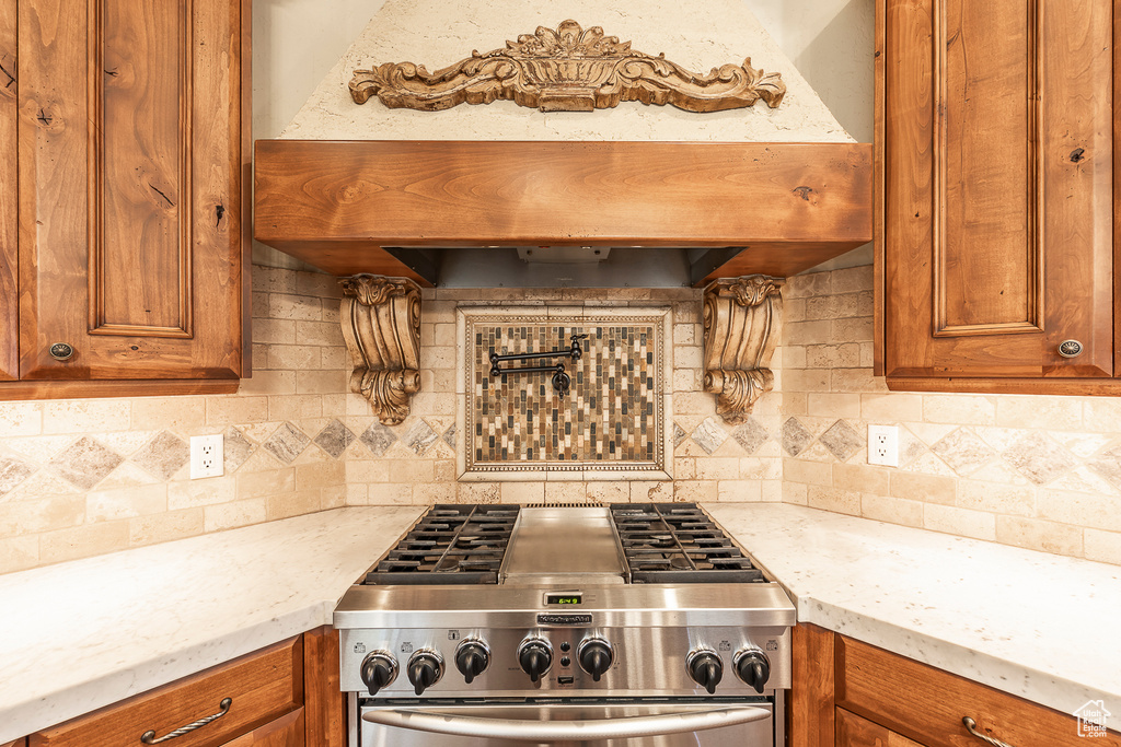 Kitchen with high end stainless steel range oven, backsplash, premium range hood, and light stone counters