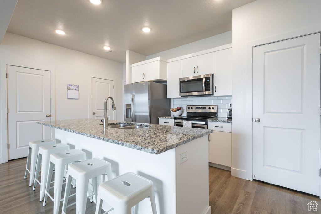 Kitchen with white cabinets, dark wood-type flooring, appliances with stainless steel finishes, a kitchen bar, and a center island with sink