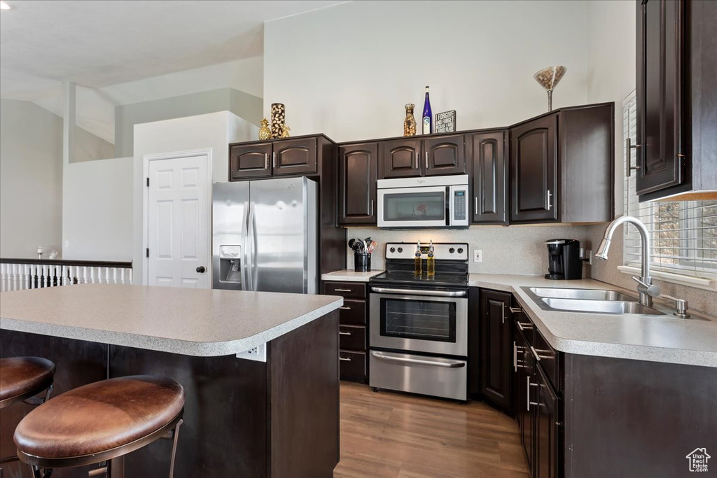 Kitchen with dark wood-type flooring, a breakfast bar area, dark brown cabinets, stainless steel appliances, and sink