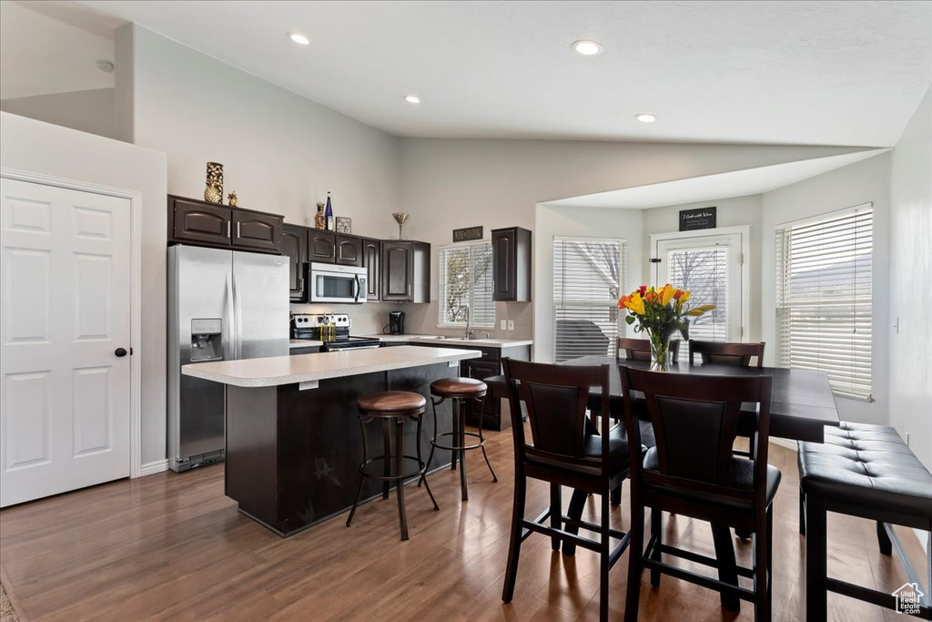 Kitchen featuring appliances with stainless steel finishes, a kitchen bar, dark hardwood / wood-style floors, a kitchen island, and dark brown cabinetry
