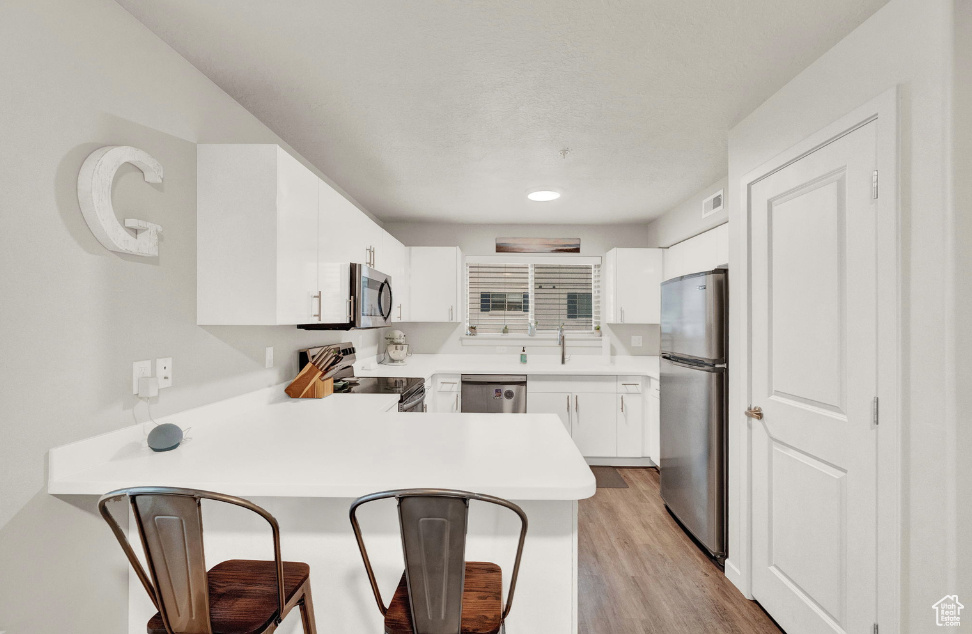 Kitchen with white cabinetry, light hardwood / wood-style flooring, stainless steel appliances, and kitchen peninsula