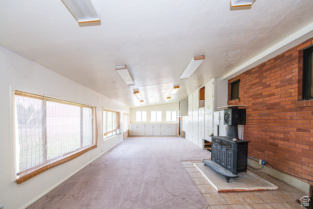 Unfurnished living room with lofted ceiling, brick wall, a wood stove, and light carpet