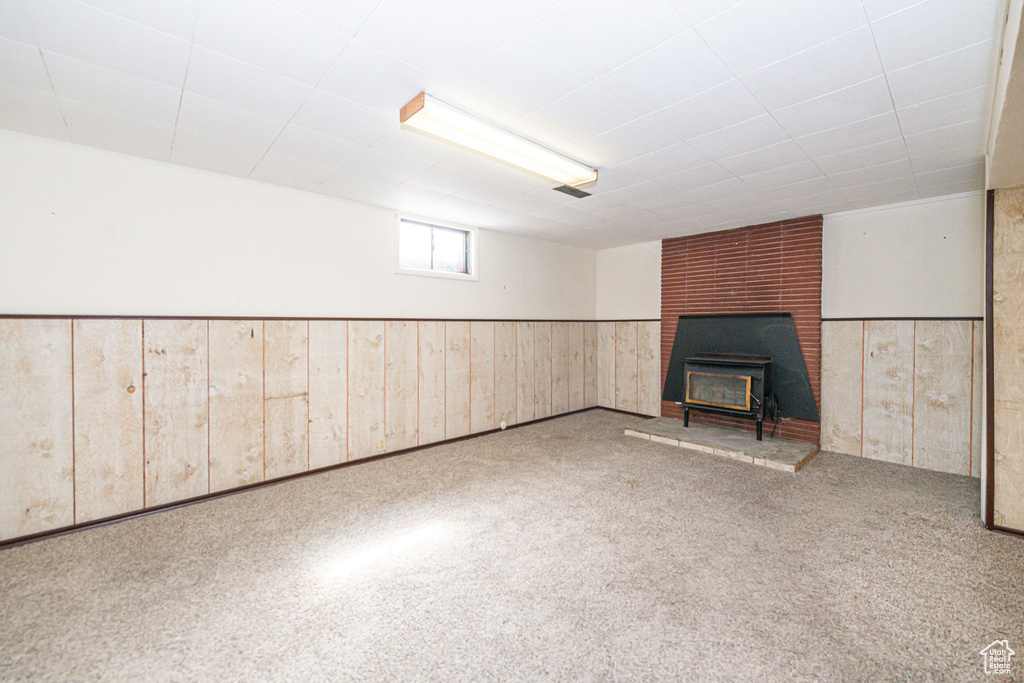 Basement featuring a wood stove, brick wall, and carpet
