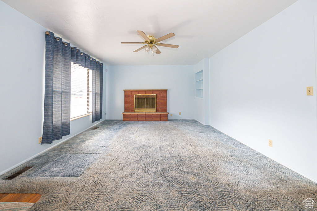 Unfurnished living room featuring ceiling fan, dark carpet, and a brick fireplace