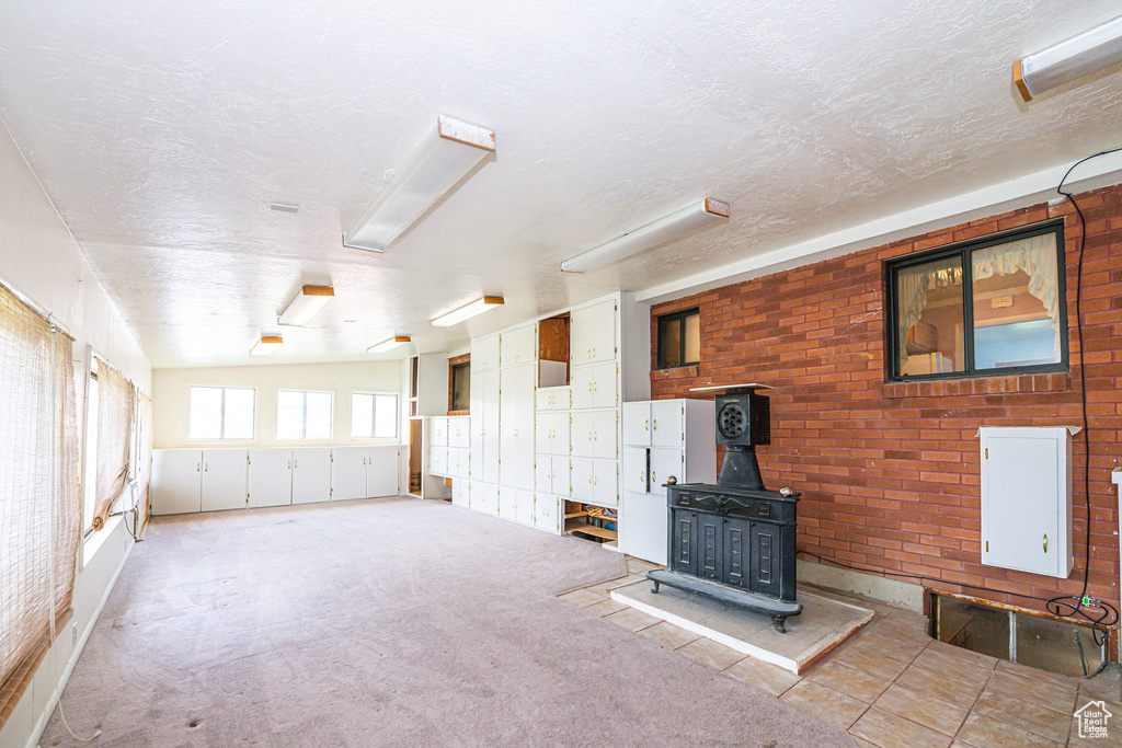 Unfurnished living room featuring a wood stove, brick wall, a textured ceiling, and light colored carpet
