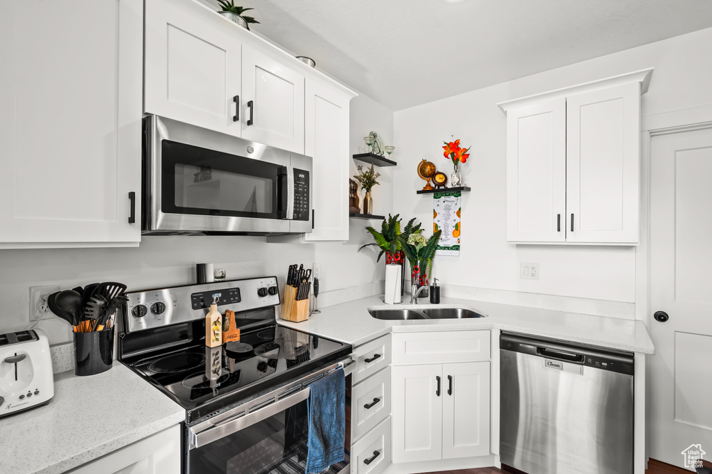 Kitchen with white cabinetry, appliances with stainless steel finishes, light stone counters, and sink