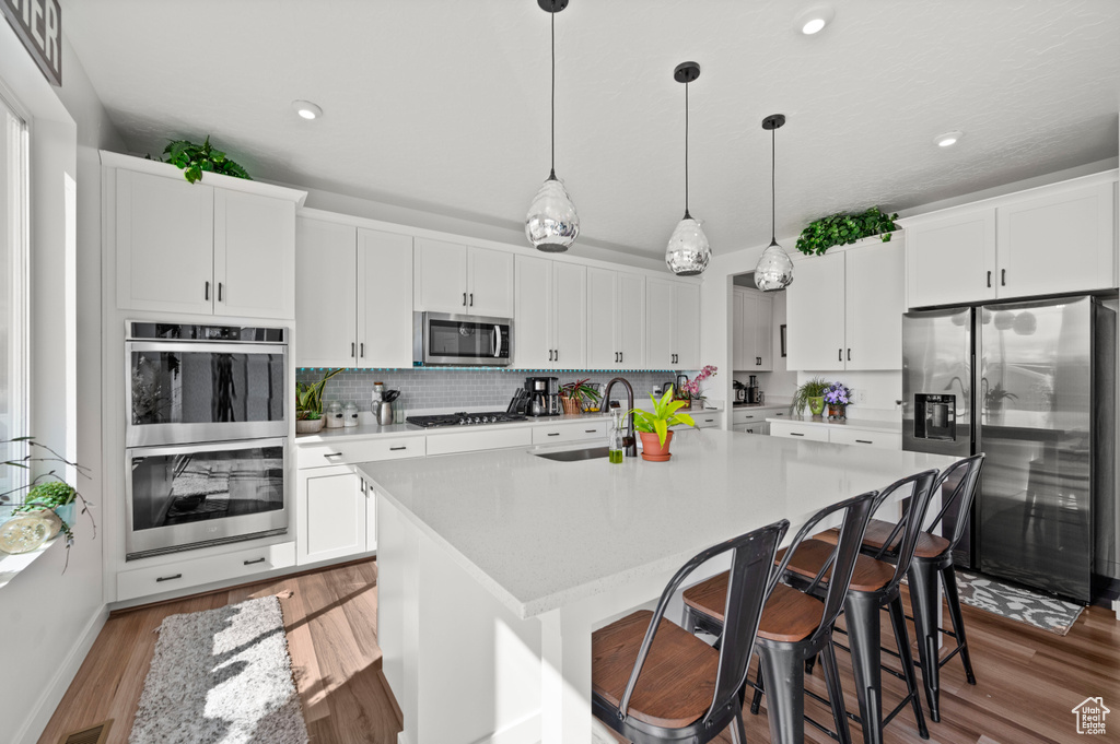 Kitchen featuring white cabinets, light wood-type flooring, decorative light fixtures, and appliances with stainless steel finishes