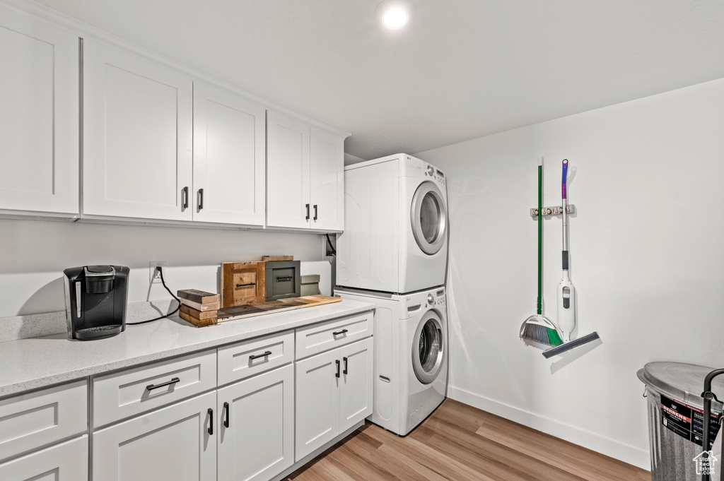 Laundry area featuring cabinets, stacked washing maching and dryer, and light hardwood / wood-style floors